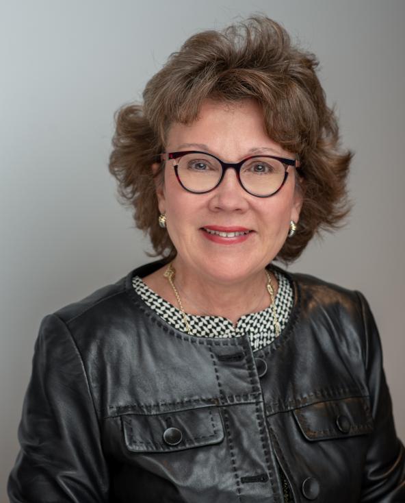 Mary Anne's Headshot. Wearing a black jacket and black and white checkered shirt