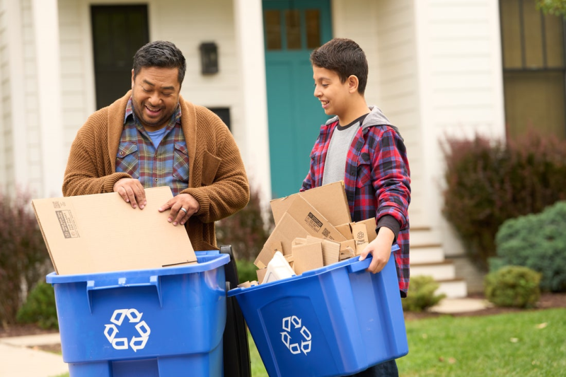 Two Consumers Holding Filled Recycling Bins Outside of Residence